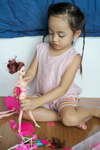 Cute girl playing with doll while sitting on floor at home