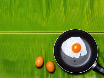 Directly above shot of eggs and fried egg in cooking pan on leaf