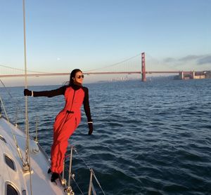 Full length of young woman on suspension bridge over sea against clear sky