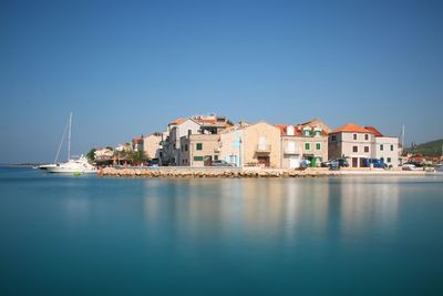 Buildings by sea against clear blue sky