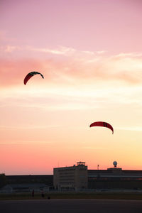 Distant view of male friends flying kites against orange sky
