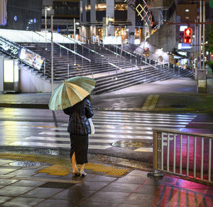 A woman holding an umbrella, waiting to cross the street in tokyo.