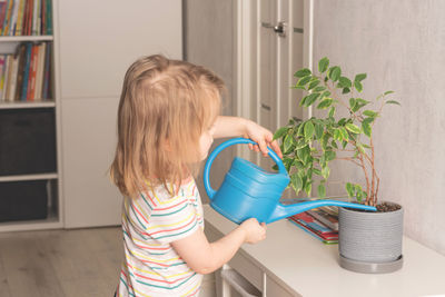 Child watering home plant with blue watering can. the environmental trend and prioritize our planet