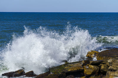 Waves splashing on rocks against sky