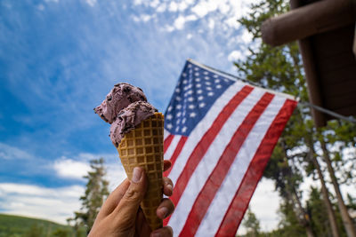 Cropped image of hand holding ice cream against sky