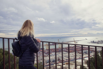 Side view of woman looking at commercial dock against cloudy sky