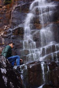 Low angle view of woman sitting on rock against waterfall