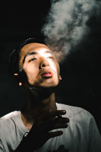 Portrait of young man smoking cigarettes with black background