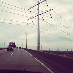 Road by electricity pylon against sky