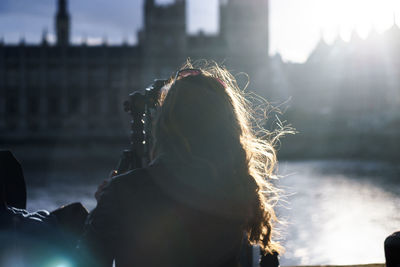 Woman standing by thames river against houses of parliament