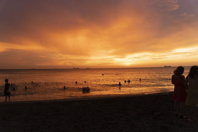 Silhouette people on beach against sky during sunset