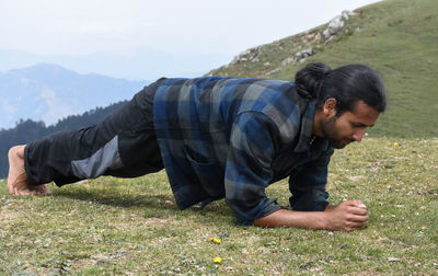 A handsome indian young man with ponytail hair doing plank exercise in the top of mountain