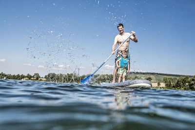 Full length of shirtless man standing in water against sky