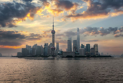 Oriental pearl tower and buildings by sea against sky during sunset