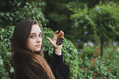 Portrait of smiling young woman holding fruits standing against plants