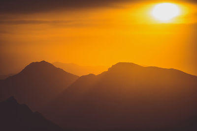 Scenic view of silhouette mountains against orange sky