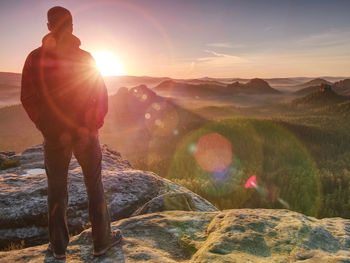 Moment of loneliness. sportsman with hands in pockets stand on the rock peak and watching sunset.