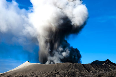 Smoke emitting from volcanic mountain against blue sky