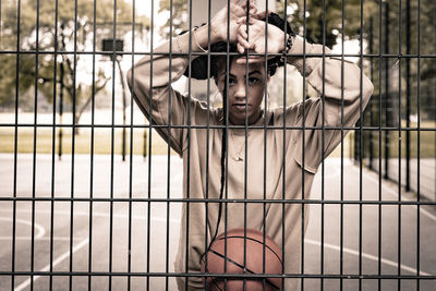 Low angle view of young woman seen through chainlink fence