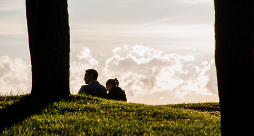 Rear view of couple sitting on field against sky