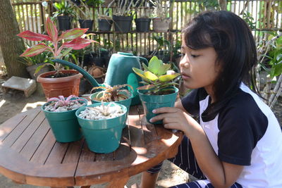 Side view of young woman sitting by potted plant on table