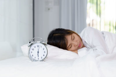 Woman sleeping by alarm clock on bed at home