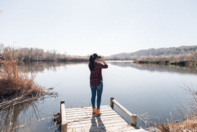 Rear view of man standing on pier over lake against sky
