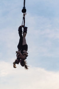 Low angle view of man climbing hanging against sky