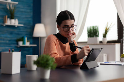 Young woman using digital tablet while sitting on table