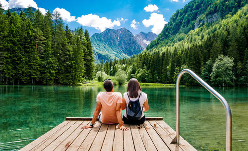 Rear view of people sitting by lake against mountains