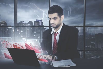 Digital composite image of businessman using laptop with various icons at office