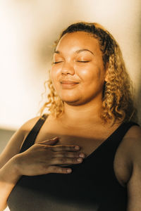 Smiling woman with hand on chest against wall