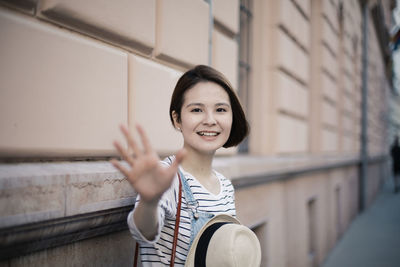 Portrait of smiling young woman gesturing against wall outdoors