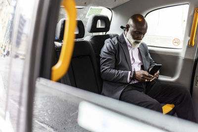 Senior businessman using mobile phone in taxi