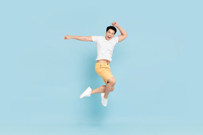 Full length of boy jumping against blue background