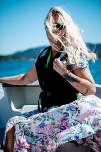 Mid adult woman wearing sunglasses while sitting in boat on lake against clear blue sky