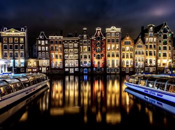 Illuminated buildings by canal in city at night