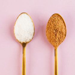 Coconut and refined white sugar in gold spoons on a pink background. minimalism. 