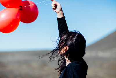 Side view of young woman holding balloons at beach