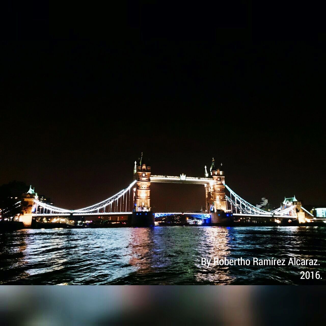 ILLUMINATED BRIDGE OVER RIVER AT NIGHT