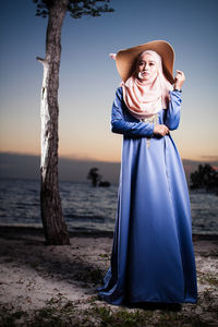 Full length of woman wearing traditional clothing while standing at beach against sky during sunset