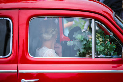 Side view of woman sitting in red car seen through window