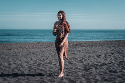 Full length of young woman at beach against sky
