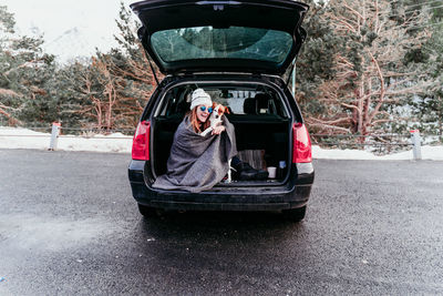 Woman holding dog while sitting in car trunk