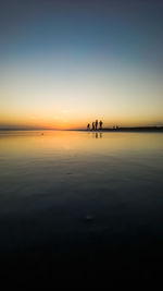 Silhouette people on sea against sky during sunset