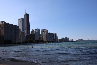 City buildings by sea against clear sky