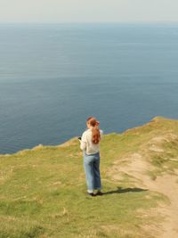 Rear view of woman standing on mountain by sea against sky