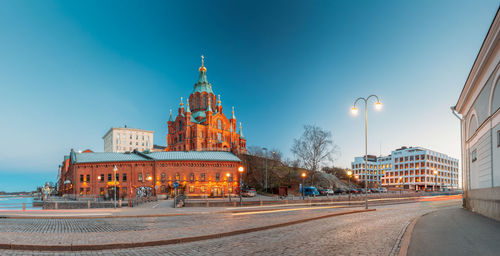 Illuminated street amidst buildings against sky at dusk