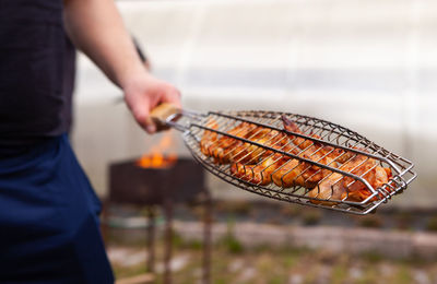 Midsection of man holding meat on barbecue grill