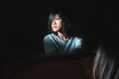 Portrait of a smiling young woman sitting against black background